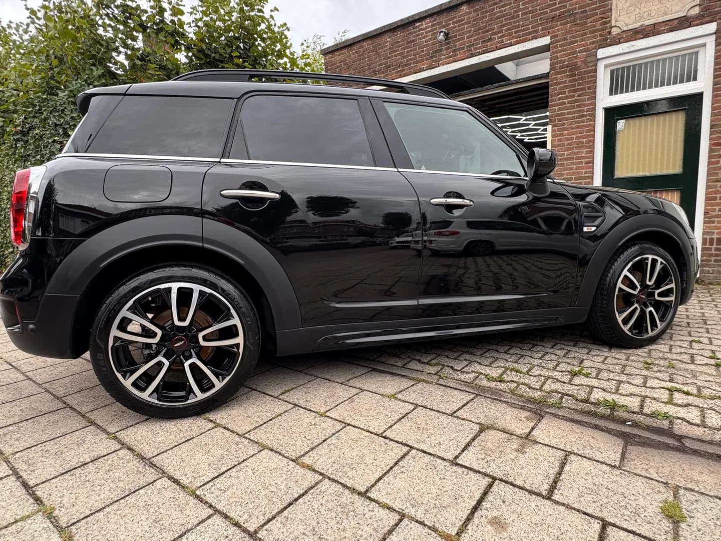 Zwarte MINI Countryman in zijaanzicht voor het atelier, met reflecties in de portieren