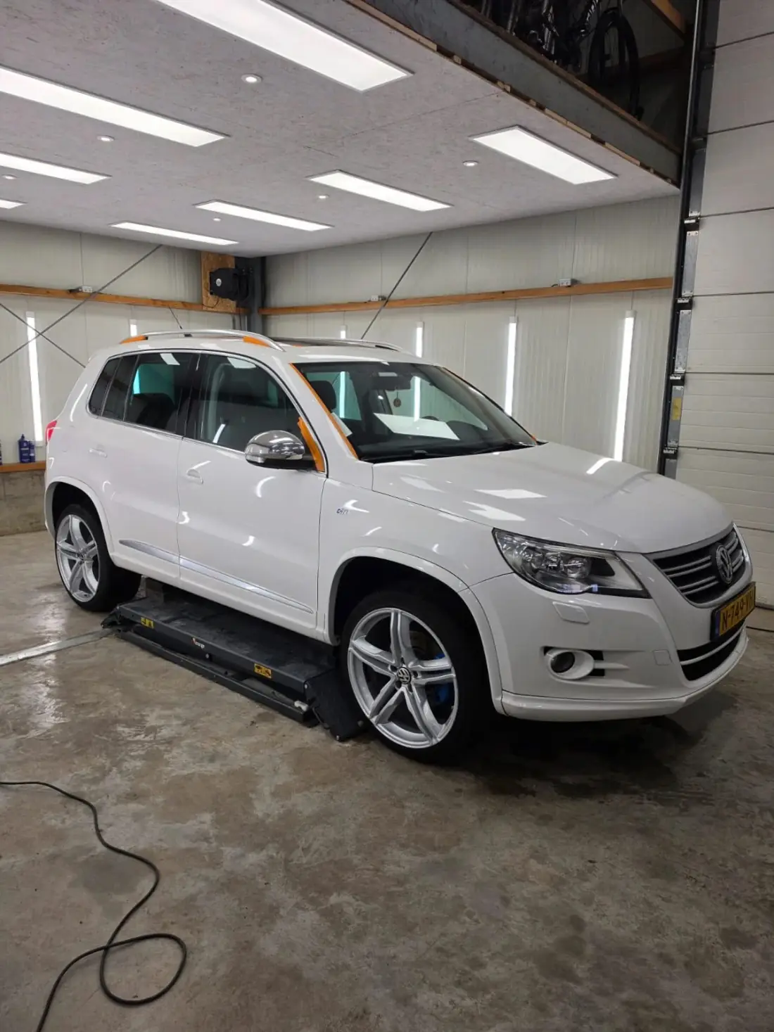 Witte Volkswagen Tiguan R-Line op de brug in de werkplaats tijdens een complete detailbeurt