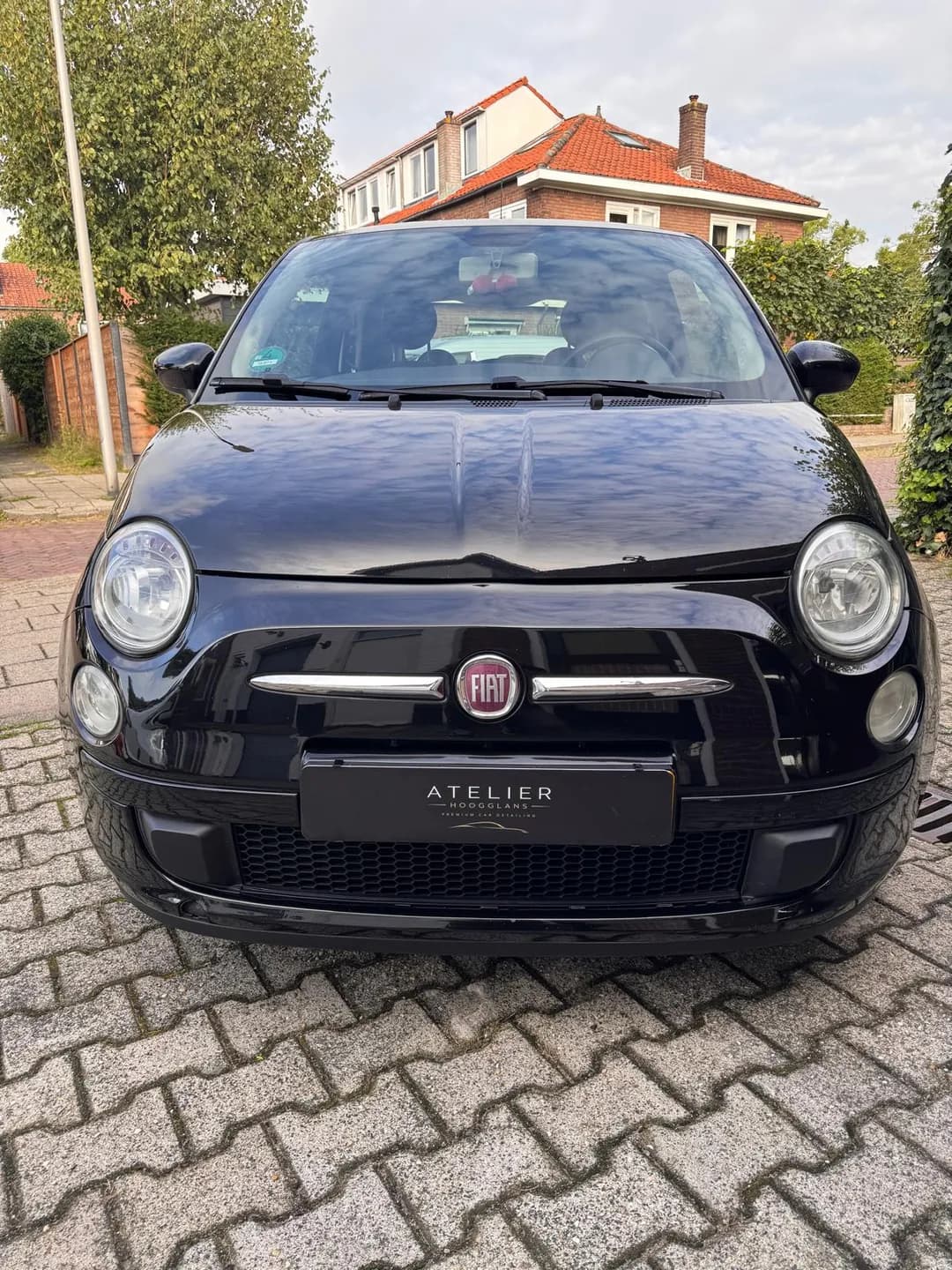 Zwarte Fiat 500 van voren met ronde koplampen en reflecties op de motorkap